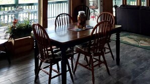 A wooden dining area with a table and chairs, large windows, and a view of the outdoors. - White River Bank Cabin!Eagle Watching, World Class Trout Fishing Off  The Dock,  (Flippin)