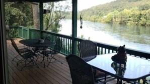 Une terrasse extérieure couverte, dotée d’une table et de chaises, qui offre une vue sur une rivière et des collines boisées.