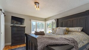 Een slaapkamer met een groot bed, een dressoir, een televisie en een raam met uitzicht op de omgeving.