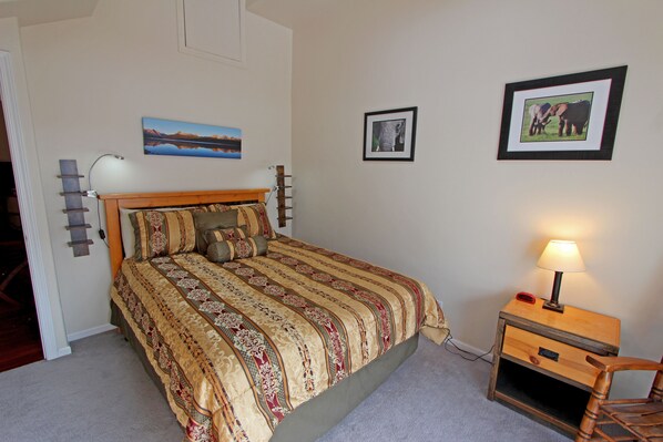 A bedroom with a large bed, a bedside table with a lamp, and two framed pictures on the wall. - Walk to Sun Valley Ski Area-River Run & Downtown - Fireplace, Hot Tub (Ketchum)