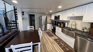 A modern kitchen with white cabinets, stainless steel appliances, and a wooden dining table with white chairs.