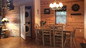 Un intérieur en bois comprenant une table et des chaises, un lustre, un lave-linge et une fenêtre avec des stores.