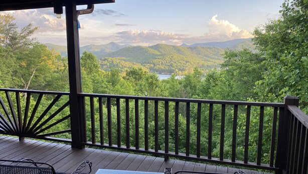 Une terrasse en bois, avec des chaises et une table en métal, offrant une vue imprenable sur un paysage verdoyant, avec des montagnes et un lac.