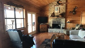 L’intérieur d’un chalet confortable, avec une cheminée en pierre, des canapés en cuir et un téléviseur.