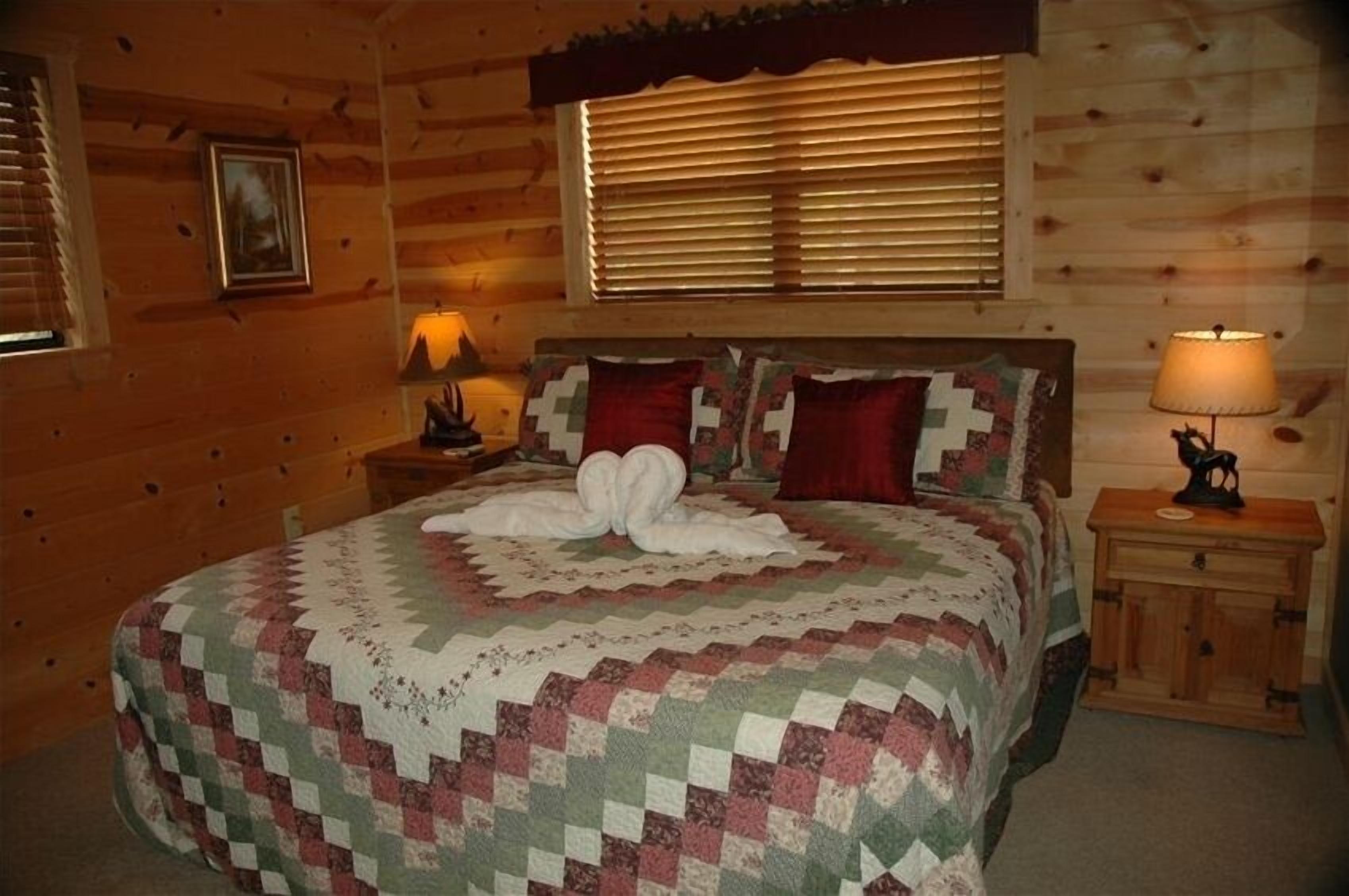 A cozy wooden cabin bedroom with a large bed, two nightstands, and a window with blinds.