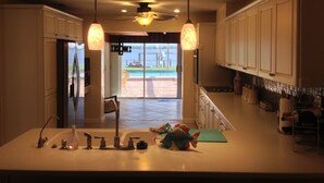 Una cocina con isla central, iluminación sobre la encimera y vistas a una piscina a través de puertas de vidrio.
