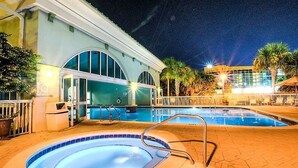 Un área de piscina con dos piscinas, una zona de estar cubierta y un edificio con ventanas arqueadas.