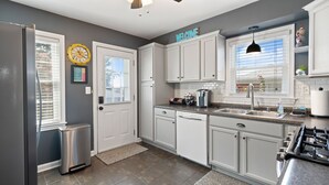 A modern kitchen with white cabinets, a stainless steel refrigerator, a dishwasher, a stove, and a ceiling fan.