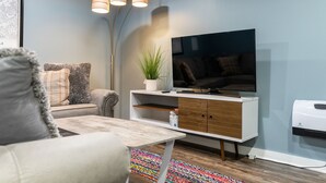 A modern living room with a flat-screen TV, a white cabinet, a sofa, and a colorful rug.