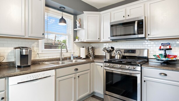 A modern kitchen with white cabinets, stainless steel appliances, a built-in microwave, and a gas stove.