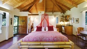 A bedroom with a large bed, wooden ceiling beams, a canopy bed, a small kitchen, and a dining area. - Tropical Romance... Lush Gardens.... in Heavenly Hana, Maui (Hāna)