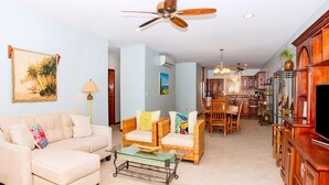A living room with a sofa, chairs, a glass coffee table, a ceiling fan, and a TV. - Oceanfront First Floor 2 Bed/2 Bath - Free use of Kayaks (San Pedro)