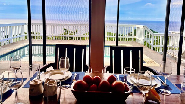 Une table à manger avec vue sur l’océan, des rampes blanches et une piscine.