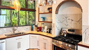 Une cuisine moderne équipée d’une cuisinière, d’un four et de divers appareils électroménagers. Une fenêtre offre une vue sur la verdure environnante.