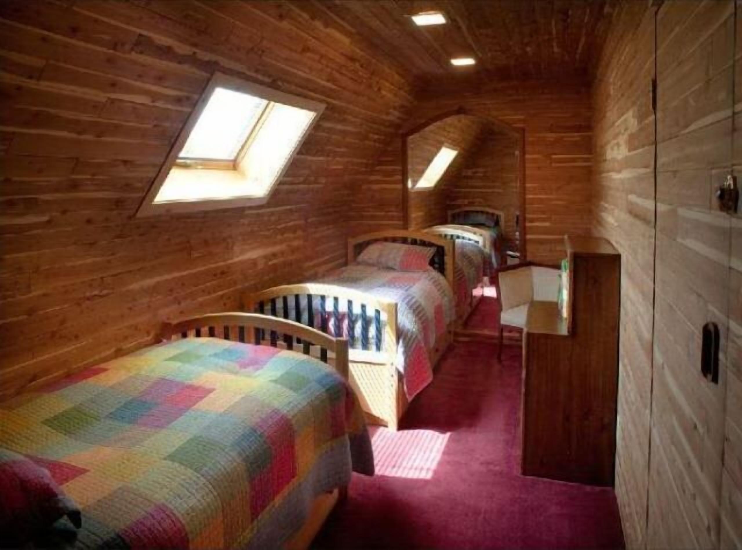 A cabin with wooden walls, two beds with colorful quilts, a small desk, and a skylight.