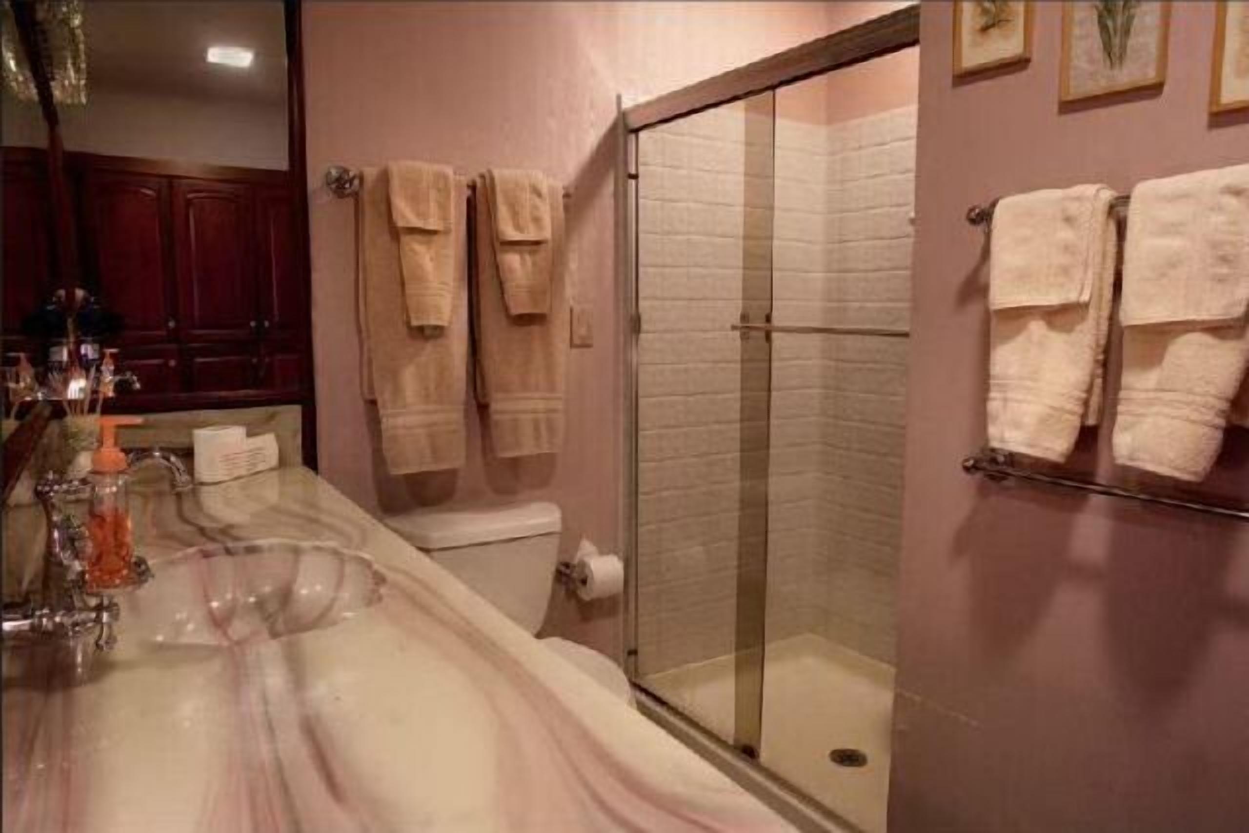 A bathroom with a marble sink, a glass shower enclosure, and multiple towels on a rack.