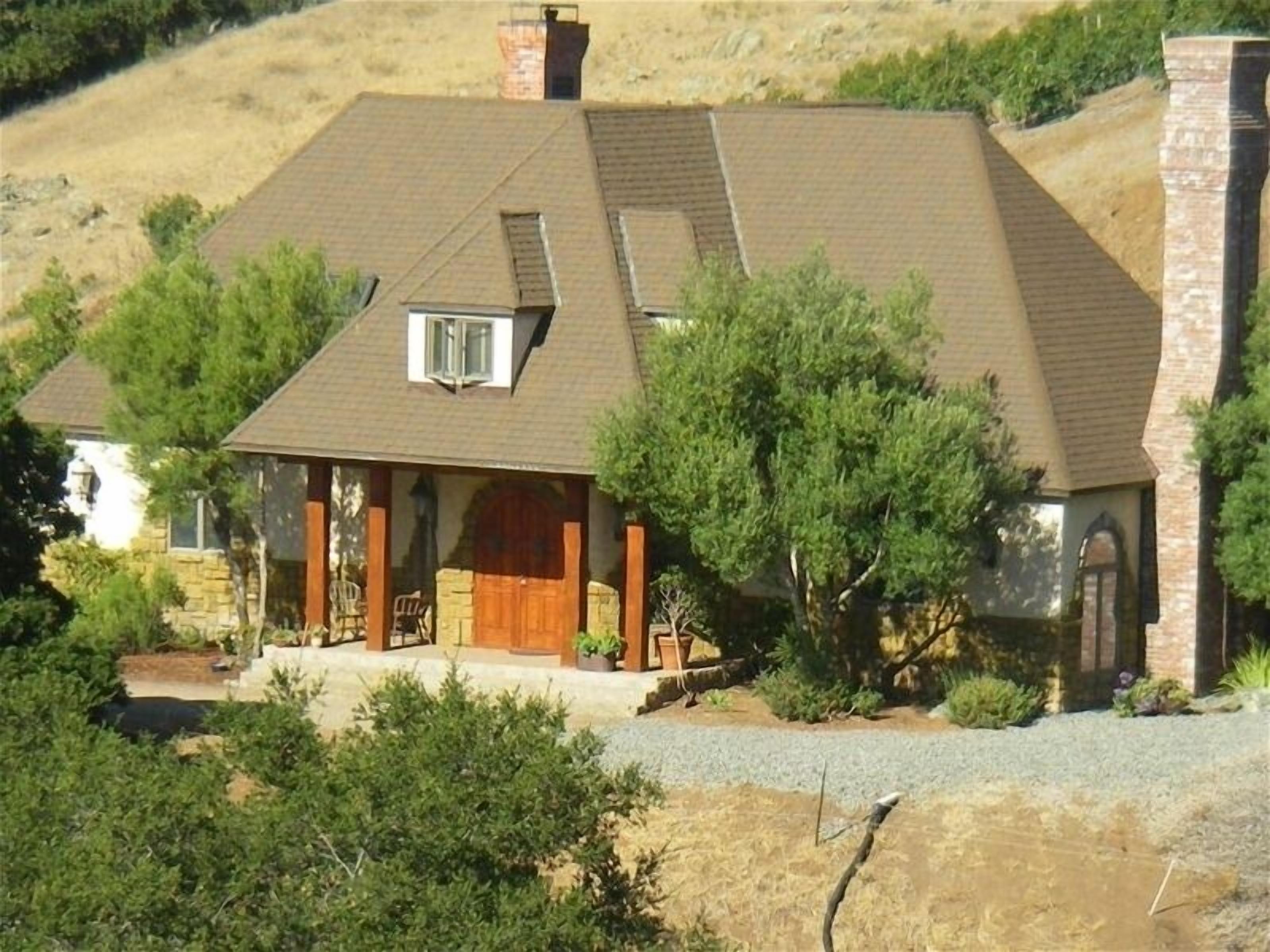 A single-story house with a sloped roof, a chimney, and a covered porch with outdoor seating.
