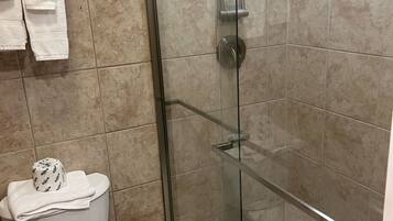 Un baño con ducha de vidrio, inodoro y estante con toallas.