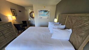 A large bed with white linens, a wooden headboard, and a painting of a beach scene on the wall. - Sarasota “Executive Waterfront Suite” A  hotel rm # 103 on Sara Bay Marina (Sarasota)