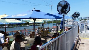 An outdoor dining area with tables and chairs, a railing, and fans. - Sarasota “Executive Waterfront Suite” A  hotel rm # 103 on Sara Bay Marina (Sarasota)