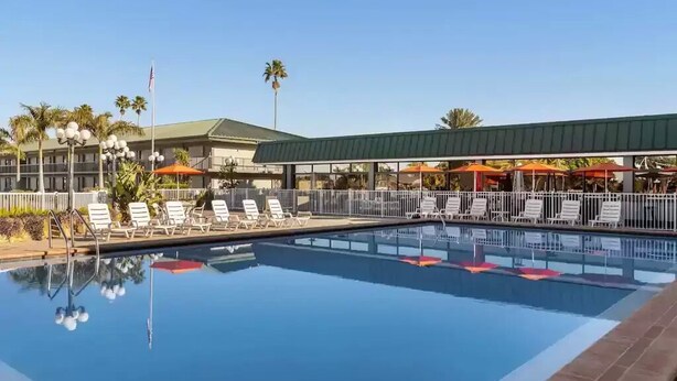 A swimming pool with lounge chairs and umbrellas, surrounded by a fence and palm trees. - Sarasota “Executive Waterfront Suite” A  hotel rm # 103 on Sara Bay Marina (Sarasota)