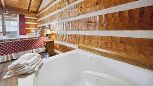 Ein Holzblockhaus-Innenraum mit einer großen Badewanne, einem Bett mit rot-weiß kariertem Überwurf und einer Holzwand mit horizontalen Planken.