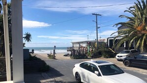 Une BMW blanche est garée dans une rue d’où l’on aperçoit la plage et l’océan au loin.