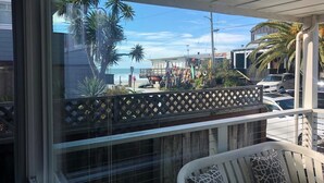 Un balcon avec vue sur la plage, les palmiers et les voitures garées.