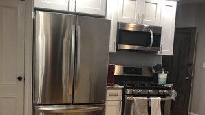 A modern kitchen with stainless steel appliances, white cabinetry, and a wooden floor.