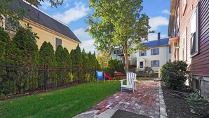 A residential backyard with a brick patio, a lawn, and a metal fence.