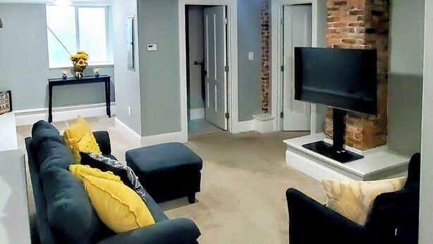 A living room with a dark-colored sofa, a TV on a brick wall, and a carpeted floor.