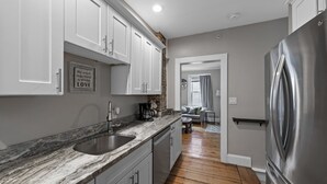 A modern kitchen with white cabinets, a stainless steel refrigerator, and a marble countertop.