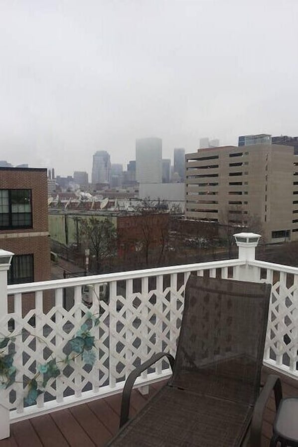A balcony with a white lattice railing, a dark-colored lounge chair, and a view of a cityscape with buildings. - LOCATION, LOCATION LOCATION, 2 Bed, 2 Bath Luxury Condo (South Boston)