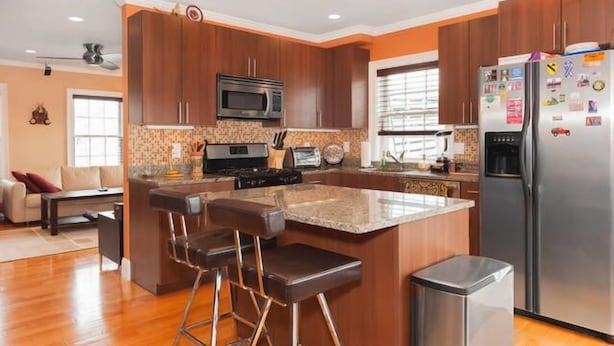 A modern kitchen with wooden cabinets, a stainless steel refrigerator, and a central island with bar stools.
