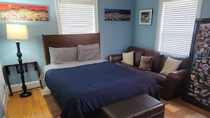 A bedroom with a bed, a desk, a chair, a ceiling fan, and a window.