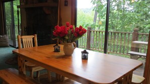 Een houten eettafel met banken, een vaas met rode bloemen en een kleine decoratie in de vorm van een huis.