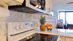 A kitchen with a white stove, a microwave above it, and a bowl of fruit on the counter.