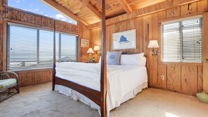 A four-poster bed in a wooden room with large windows and a ceiling fan.