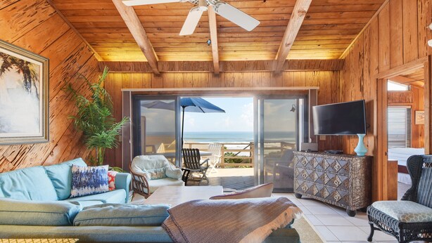 A wooden interior with a sofa, chairs, a television, and a view to the outside.