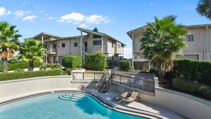 A swimming pool with a curved design, surrounded by a landscaped area with palm trees and a building with a balcony.