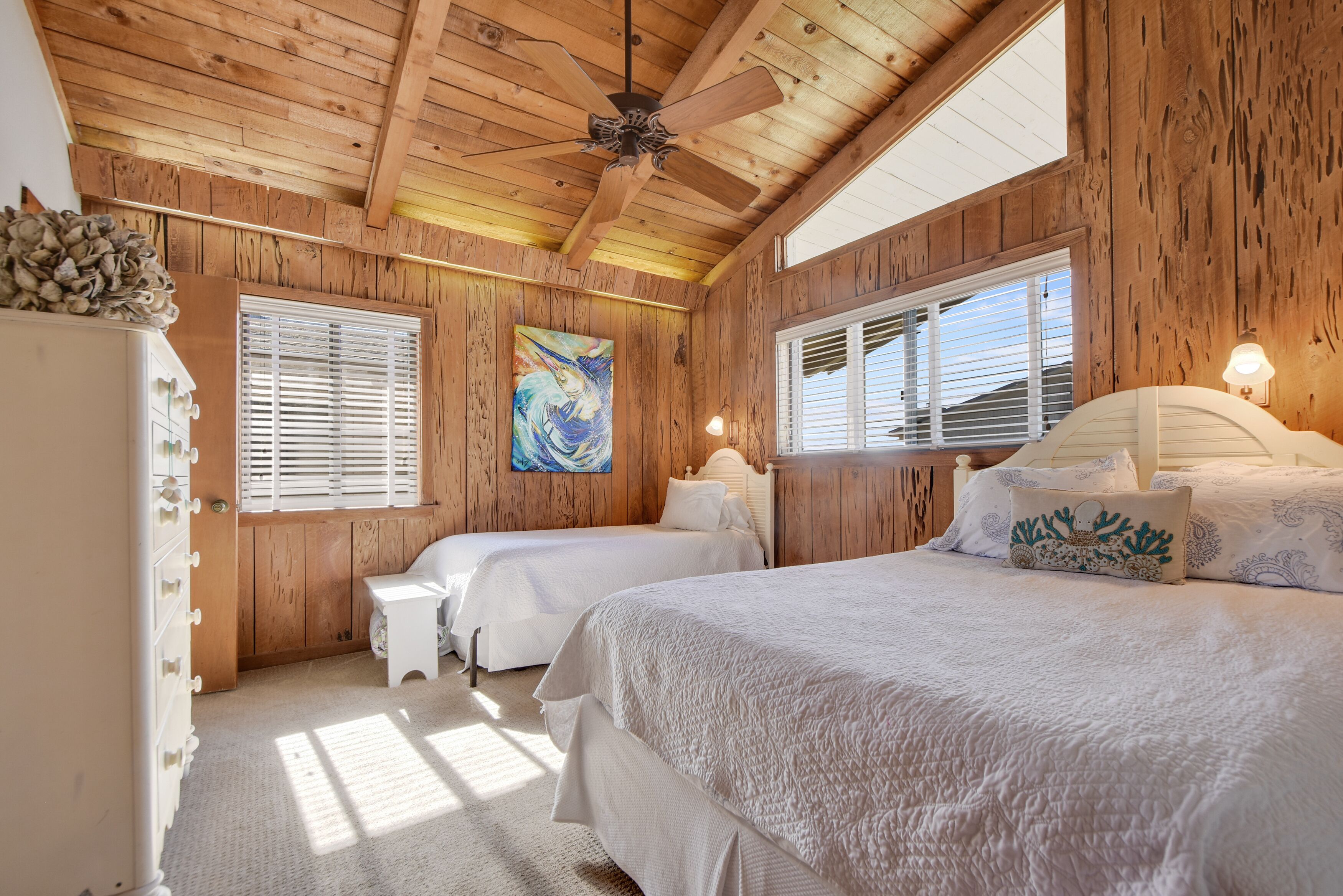 Una camera da letto con pareti in legno, due letti, una ventola a soffitto e un quadro appeso al muro.