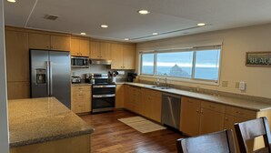 A modern kitchen with wooden cabinets, stainless steel appliances, a built-in microwave, and a view of the ocean through a large window. - Welcome to the Harris Beach House! ON the beach with private beach access. (Brookings)