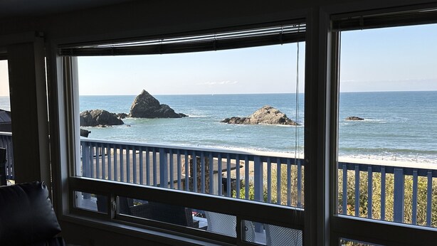 A room with a large window overlooking a beach with rocky outcrops and a wooden deck. - Welcome to the Harris Beach House! ON the beach with private beach access. (Brookings)