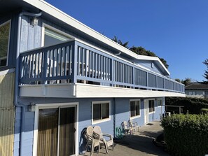 A two-story building with a balcony, a sliding glass door, and a small patio area with chairs and a hose. - Welcome to the Harris Beach House! ON the beach with private beach access. (Brookings)