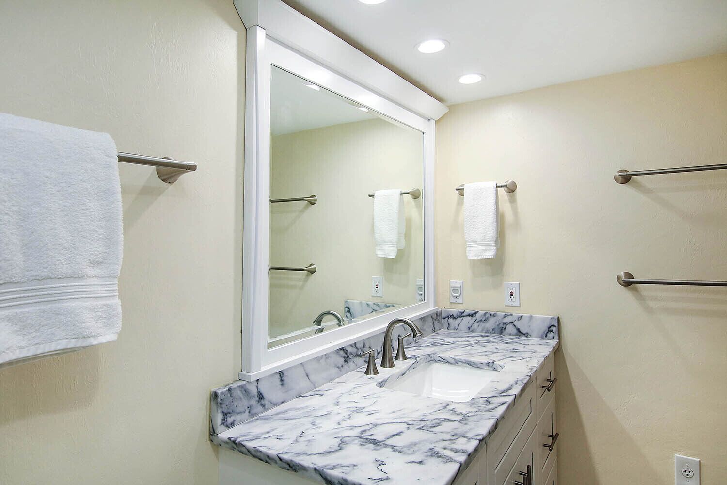 A bathroom with a marble sink, a large mirror, and towel racks.