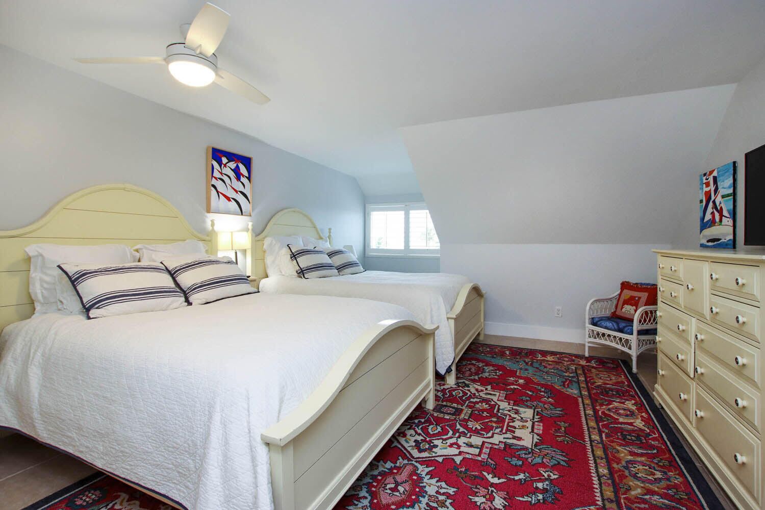 A bedroom with two beds, a ceiling fan, a dresser, and a patterned rug.