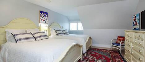 A bedroom with two beds, a ceiling fan, a dresser, and a patterned rug.