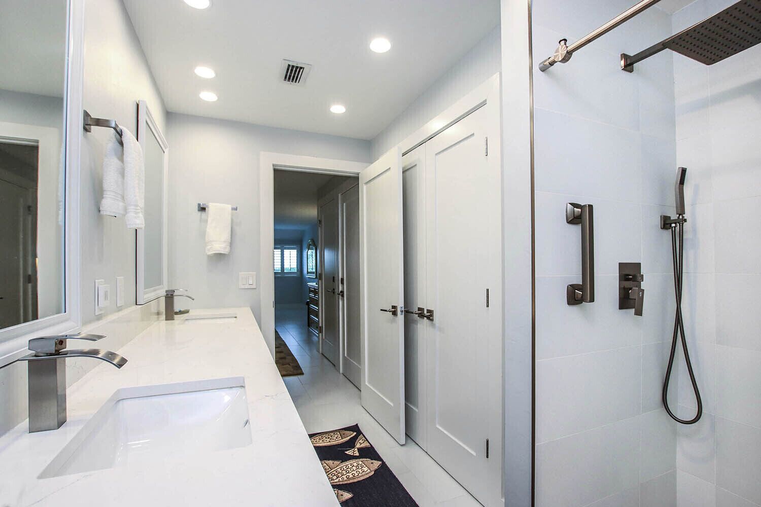 A modern bathroom with a large mirror, dual sinks, and a walk-in shower.
