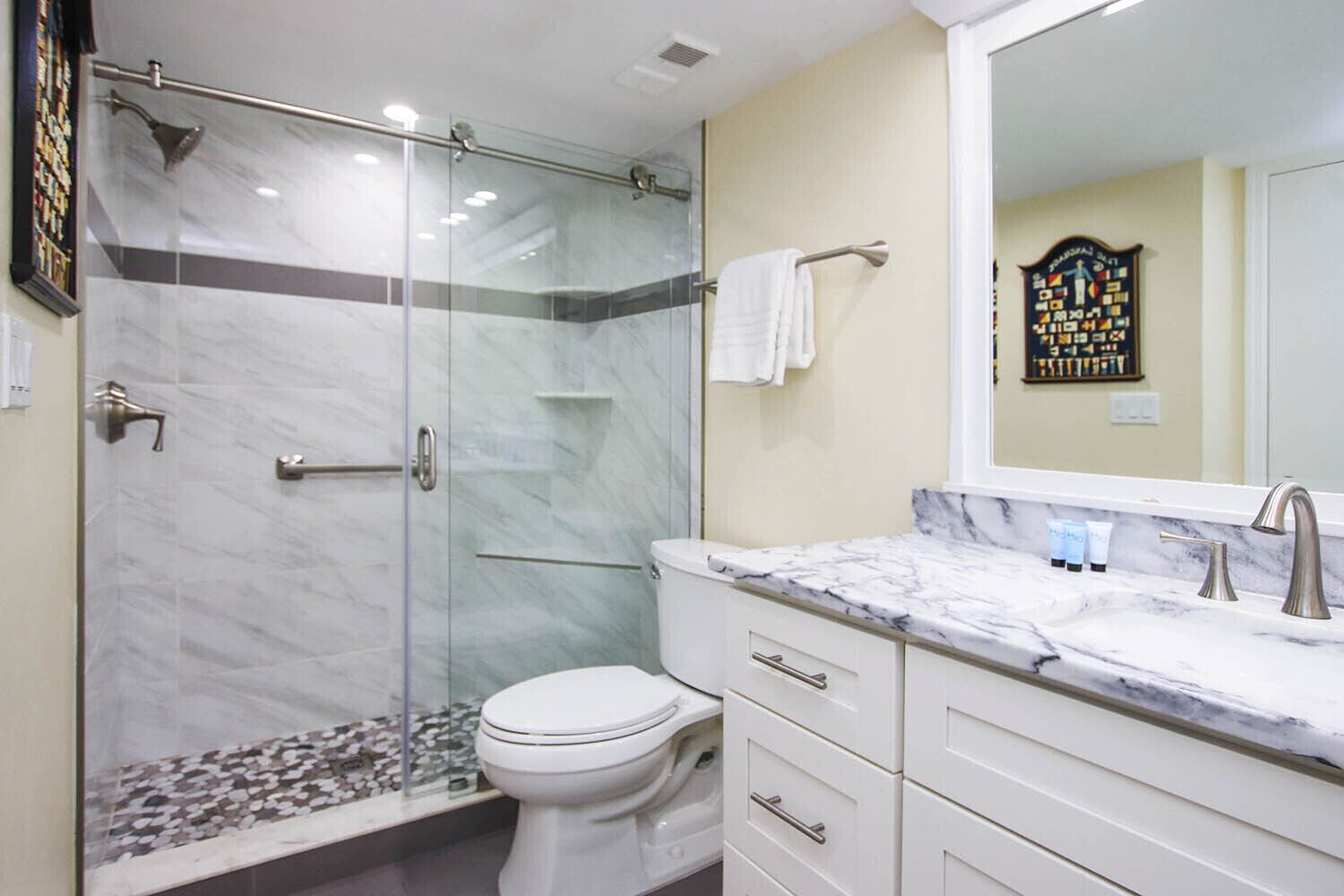 A modern bathroom with a glass-enclosed shower, a white toilet, and a marble countertop with a sink and vanity.