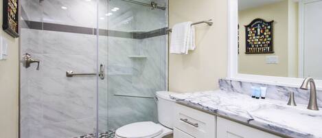 A modern bathroom with a glass-enclosed shower, a white toilet, and a marble countertop with a sink and vanity.